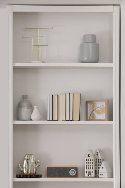 Stylish shelves with different decor elements in room. Interior design