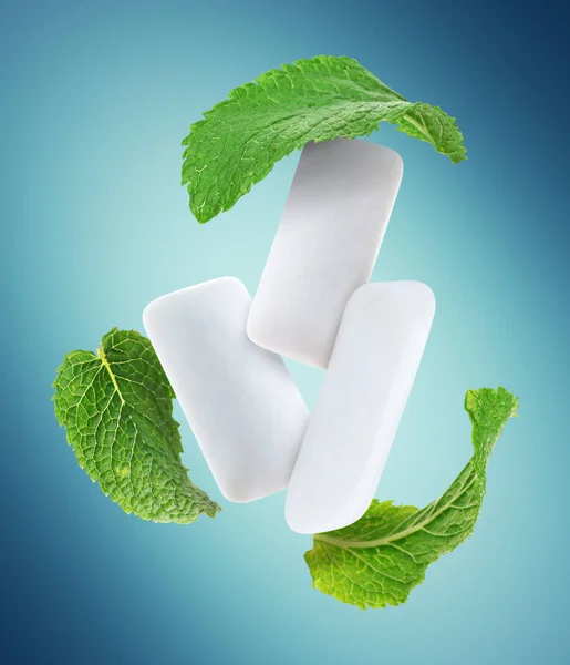 Fresh mint leaves and chewing gum pads flying on light blue background