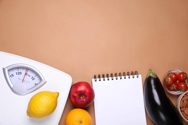 Scales, notebook, fresh fruits and vegetables on light brown background, flat lay with space for text. Low glycemic index diet
