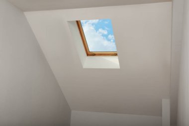 Skylight roof window and lamps on slanted ceiling in attic room, low angle view