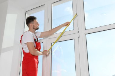 İçeride bantla pencereyi ölçen üniformalı bir işçi. Patenler kurulumu engelliyor