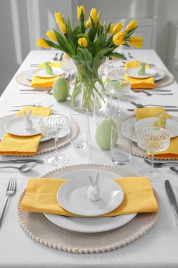 Festive table setting with glasses, painted eggs and vase of tulips. Easter celebration