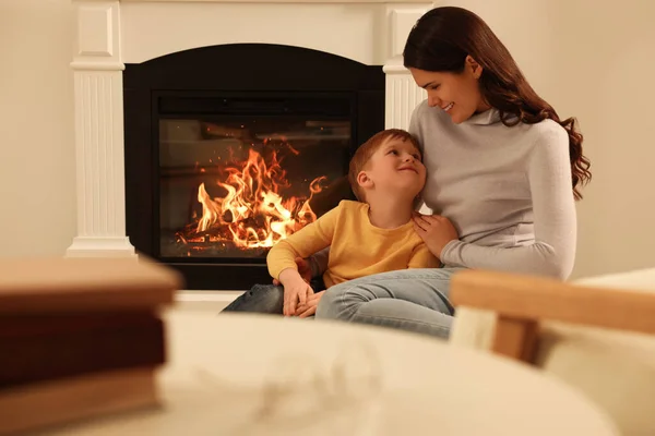 Happy mother and son spending time together near fireplace at home