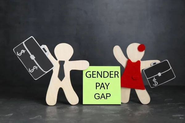 Gender pay gap. Wooden figures of man and woman on black table