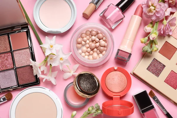 Flat lay composition with different makeup products and beautiful flowers on pink background