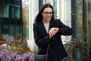 Emotional woman checking time on watch outdoors. Being late concept