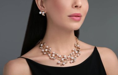 Koyu gri arka planda zarif mücevherleri olan genç bir kadın. Yakın plan.