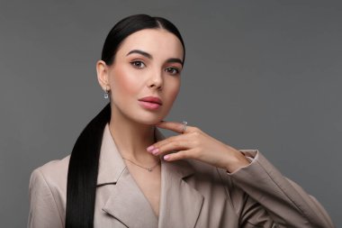 Koyu gri arka planda zarif mücevherleri olan güzel bir genç kadın.