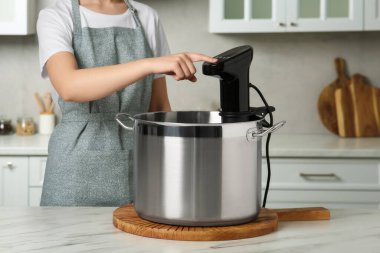 Mutfaktaki masada termal dalış sirkülatörü kullanan bir kadın, yakın plan. Sos vide pişirme