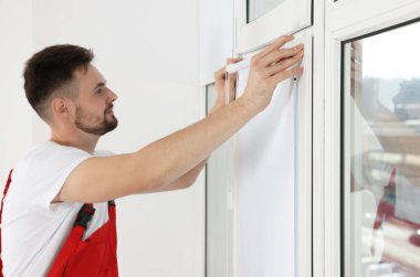 Üniformalı işçiler paten penceresi kuruyor. Kapalı alanda kör, ellere odaklanıyor.