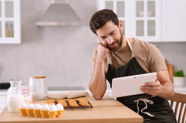 Yeni pişmiş kurabiyeli bir adam mutfakta tabletten çevrimiçi yemek kursunu izliyor.