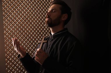 Cüppeli Katolik rahip haç tutuyor ve günah çıkarırken Tanrı 'ya dua ediyor.