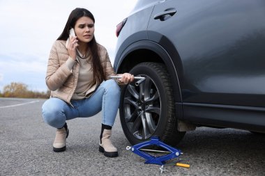 Worried young woman calling car service. Tire puncture