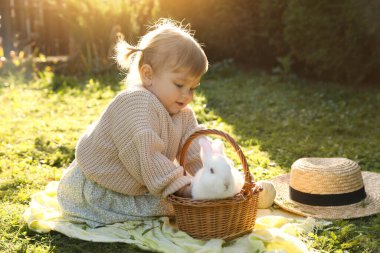 Cute little girl with adorable rabbit on green grass outdoors