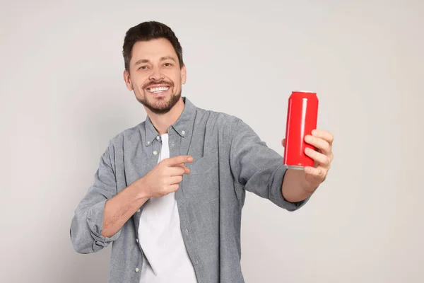Happy man holding red tin can with beverage on light grey background