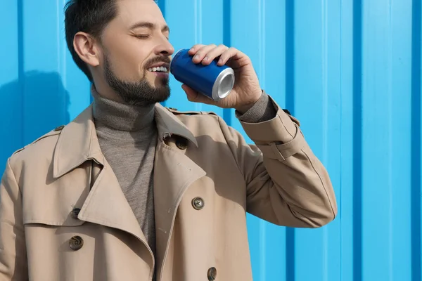Handsome man drinking from tin can near light blue wall. Space for text