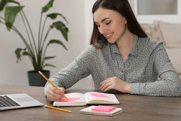 Woman with notebook and sticky note at wooden table indoors
