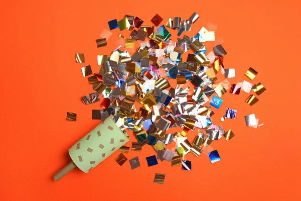 Party popper and colorful confetti on orange background, flat lay