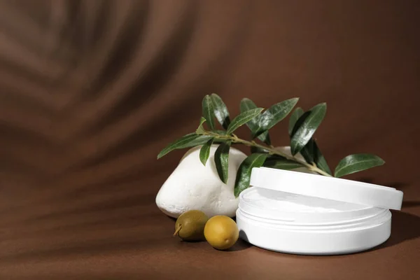 Jar of natural cream, stone and olives on brown background, space for text. Cosmetic products