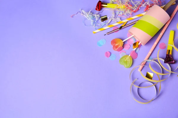 Party popper, lollipops and festive decor on violet background, flat lay