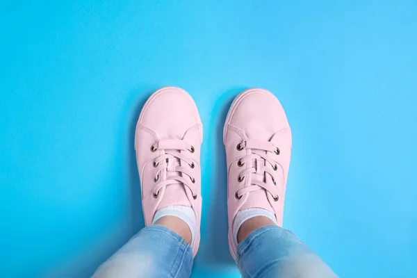 Woman in stylish sneakers standing on light blue background, top view