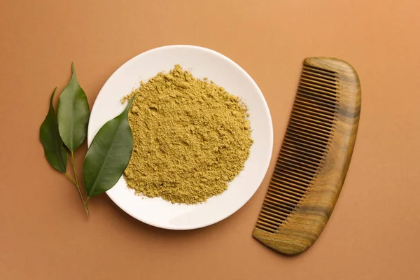 Henna powder, comb and green leaves on coral background, flat lay. Natural hair coloring