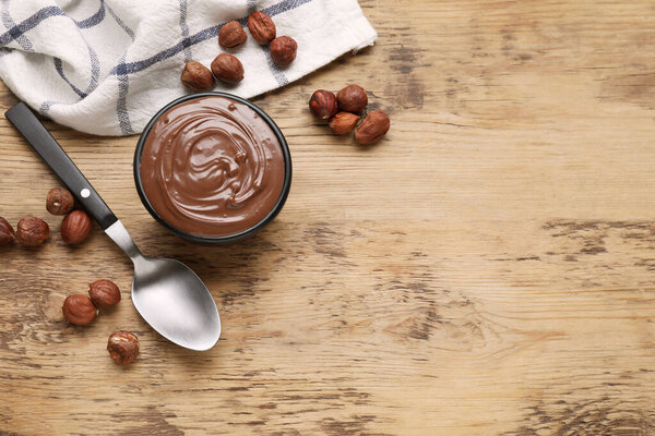 Bowl with delicious chocolate paste and nuts on wooden table, flat lay. Space for text