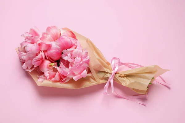 Beautiful bouquet of peonies wrapped in paper on pink background, top view