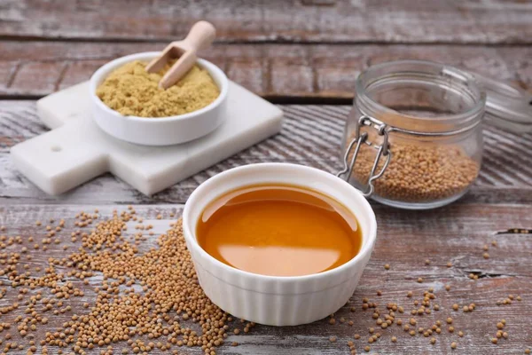 Stock image Bowl of natural oil, mustard seeds and powder on wooden table