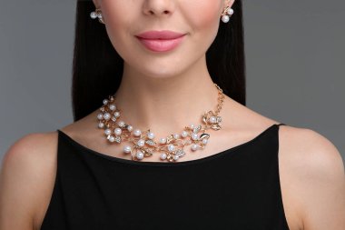 Koyu gri arka planda zarif mücevherleri olan genç bir kadın. Yakın plan.