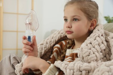 Evde nefes almak için nebulizör tutan küçük kız.