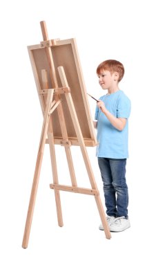 Beyaz arka planda resim yapan küçük bir çocuk. Tuvali tutmak için resim sehpası kullanılıyor