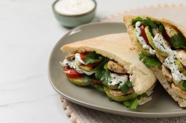 Delicious pita sandwiches with grilled vegetables and sour cream sauce on white table, closeup