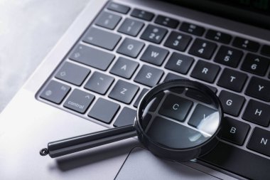 Büyüteç ve modern laptop açık gri masada, yakın plan.