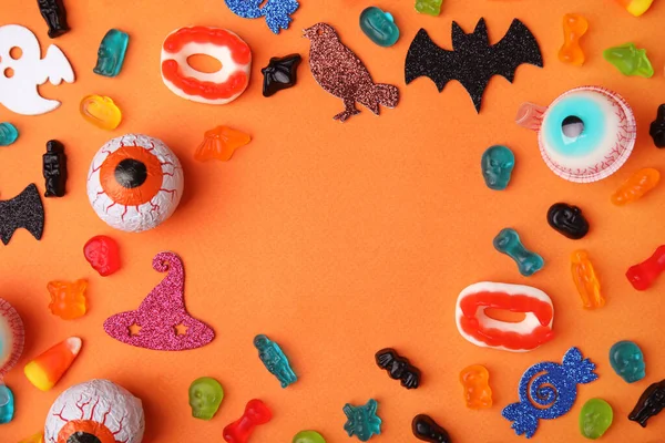 Rahmen Aus Leckeren Bonbons Und Halloween Dekorationen Auf Orangefarbenem Hintergrund — Stockfoto