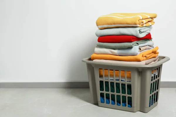 Plastic laundry basket with clean clothes on floor indoors, space for text