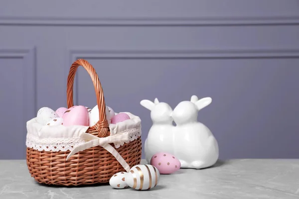 Kosz Wielkanocny Wieloma Malowanymi Jajkami Figurą Królików Szarym Stole Teksturowanym — Zdjęcie stockowe