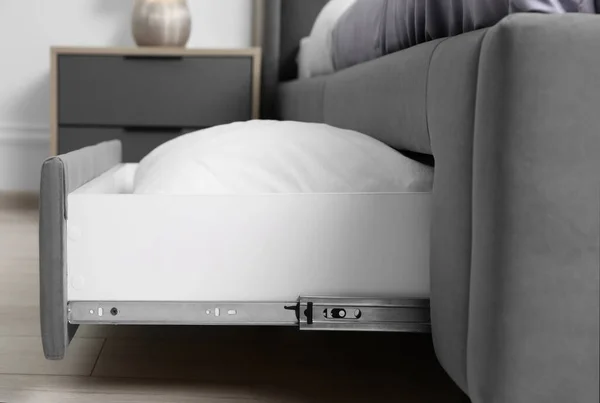Storage drawer with white pillow under modern bed in room
