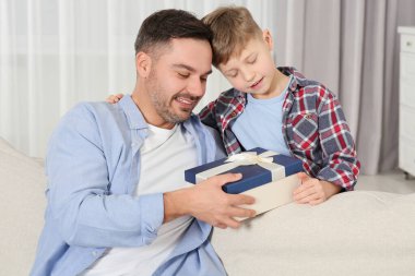 Sevimli küçük çocuk, babasıyla evdeki kanepede hediyesini sunuyor.