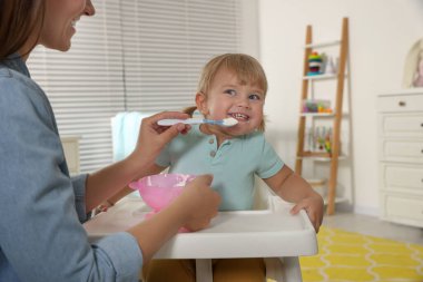 Mother feeding her cute little child with yogurt at home