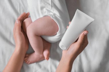Mother with cream near little baby on bed, top view