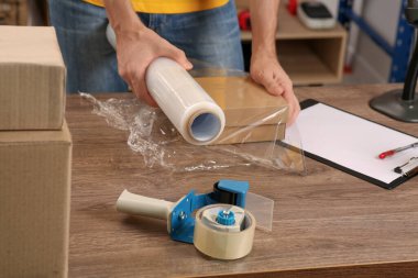 Post office worker wrapping parcel in stretch film at counter indoors, closeup
