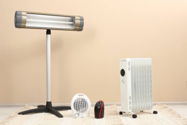 Bej duvarın yanındaki zeminde farklı modern elektrikli ısıtıcılar var.
