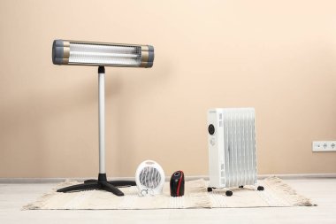 Different modern electric heaters on floor near beige wall indoors clipart
