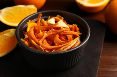 Bowl with dry orange peels and fresh fruits on wooden table, closeup