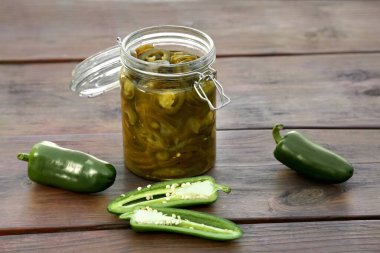 Fresh and pickled green jalapeno peppers on wooden table