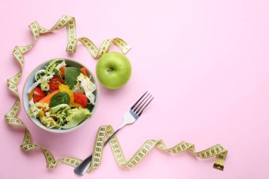 Mezura, salata, pembe arka planda elma ve çatal, düz yatak. Metin için boşluk