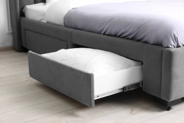 Modern yatağın altında beyaz yastıklı bir depo çekmecesi.