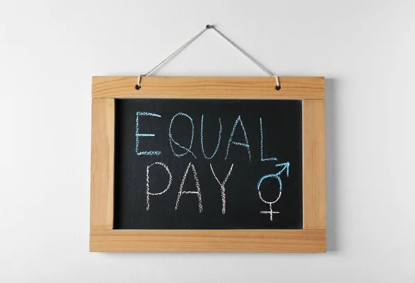 Blackboard with words Equal Pay and gender symbols hanging on white wall