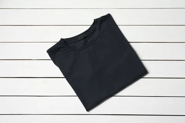 Stylish black T-shirt on white wooden table, top view